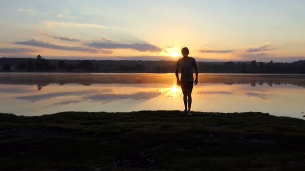 Ung man går från en sjö till en kameraman vid solnedgången i slo-mo — Stockvideo