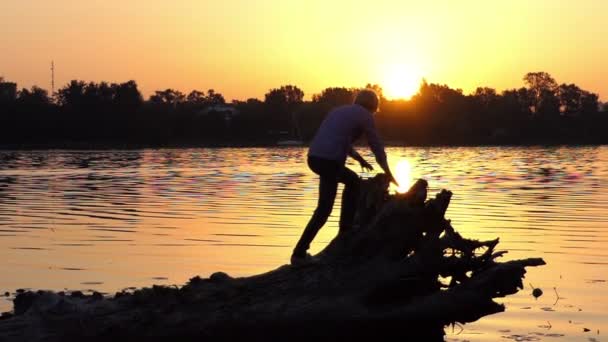 Молодой человек взбирается на корни деревьев на берегу озера в сло-мо — стоковое видео