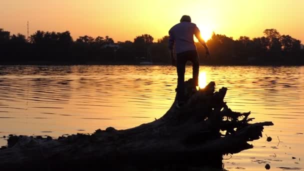 Hombre alegre sube las raíces del árbol en una orilla del lago en slo-mo — Vídeos de Stock