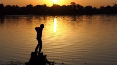 Heyecanlı adam slo-mo gün batımında bir göl kıyısında iki el yükseltir