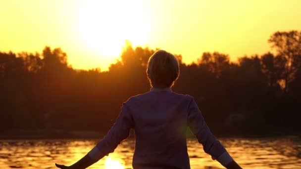 Feliz hombre mantiene levanta el puño en una orilla del lago al atardecer en slo-mo — Vídeos de Stock