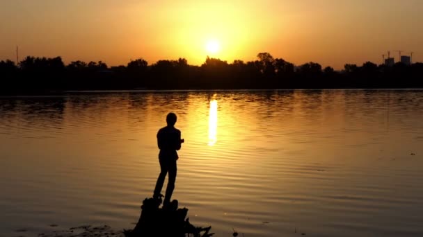 Homem romântico fica em uma margem do lago ao pôr do sol em slo-mo — Vídeo de Stock