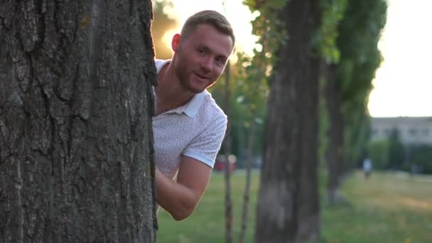 Young man playfully peeks out from behind a tree in slow motion — Stock Video