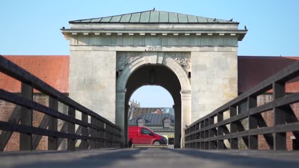 鳩が飛ぶ旧市街への門と橋。門の近くで赤い車が動く. — ストック動画