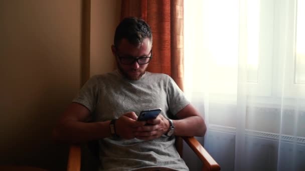 Uomo con occhiali, capelli rossi, orologio si siede sulla sedia e digitare il suo telefono . — Video Stock