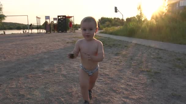 A boy in swimming shorts and a cone in his hand smiles at sunset — Stock Video