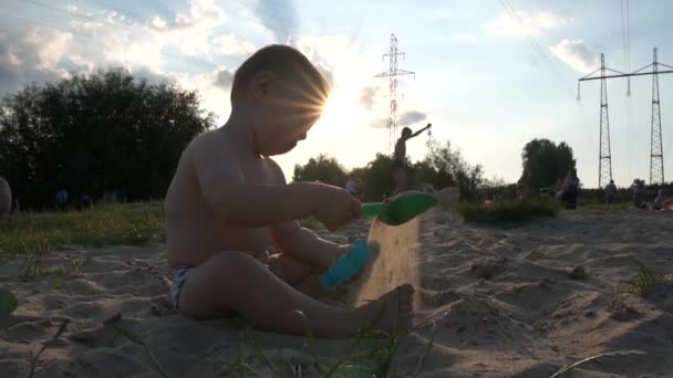 パワーライン近くのシティビーチ-小さな男の子が座ってバケツとシャベルで遊んでいます — ストック動画