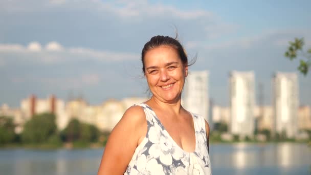 Porträt einer gewöhnlichen Frau mittleren Alters, die auf dem Hintergrund des Sees lächelt. — Stockvideo