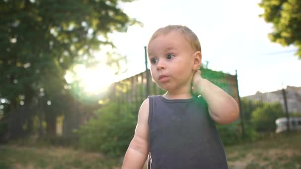 Egy két éves, ősz hajú fiú áll a játszótéren, és gondolkodik valamin., — Stock videók