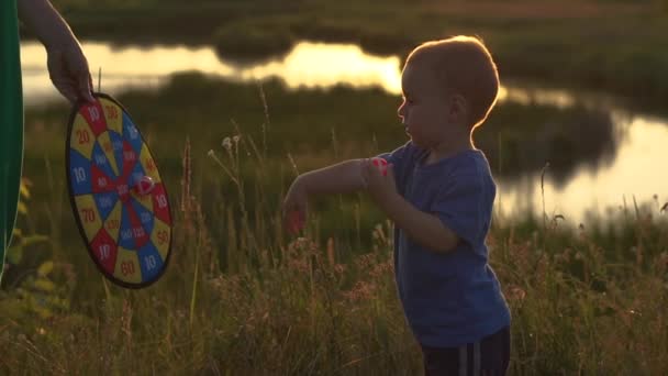 Cámara lenta - niño alegre jugar con bolas de velcro al atardecer, lanza bolas en el blanco . — Vídeo de stock