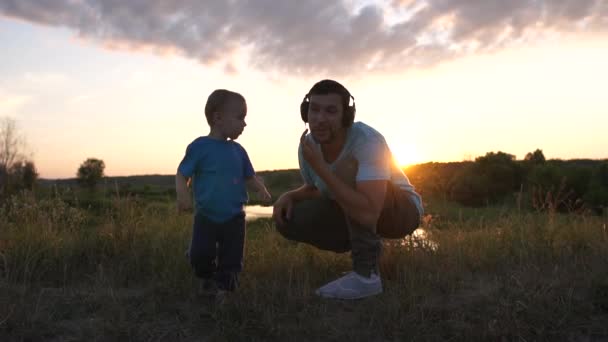 Сан цілує свого батька, який слухає музику на заході сонця в повільному темпі. — стокове відео