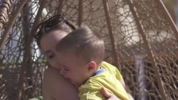 Gelukkig moeder zitten en knuffelen haar kind op zee resort in slo-mo — Stockvideo