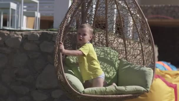 Playing boy swaying in a wattled swing in summer in slo-mo — Stock Video