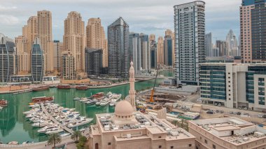 Dubai Marina 'daki yatlar El-Rahim Camii' nin ve konut kulelerinin ve gökdelenlerin yan tarafındaki yatlar gece gündüz gökdelenler.