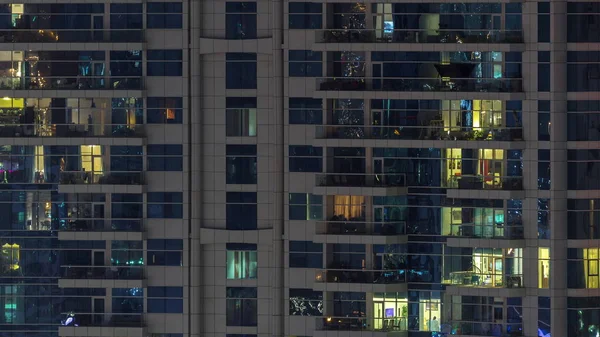 Fileiras de janelas brilhantes com pessoas no prédio de apartamentos à noite . — Fotografia de Stock