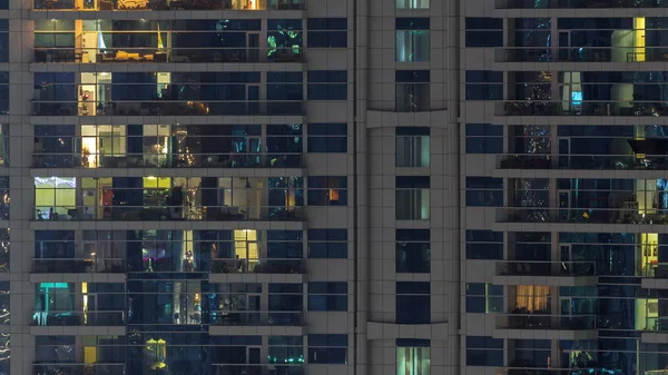 Filas de ventanas brillantes con gente en el edificio de apartamentos por la noche . — Foto de Stock