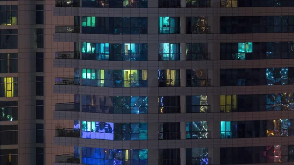 Filas de ventanas brillantes con gente en el edificio de apartamentos por la noche . —  Fotos de Stock