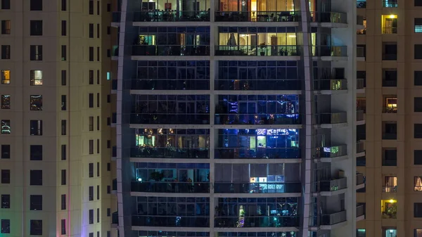 Rijen van gloeiende ramen met mensen in appartementencomplex 's nachts. — Stockfoto