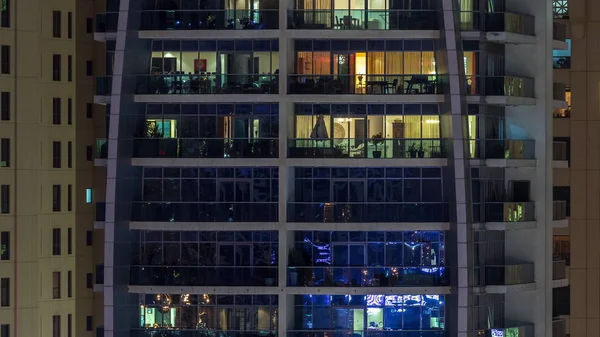 Reihen glühender Fenster mit Menschen in Mehrfamilienhaus in der Nacht. — Stockfoto