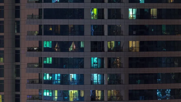 Rijen van gloeiende ramen met mensen in appartementencomplex 's nachts. — Stockfoto
