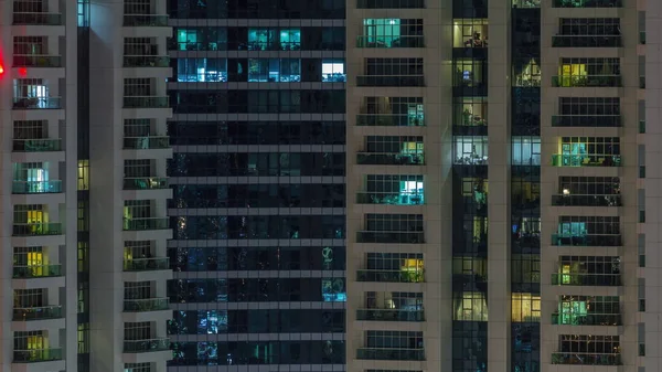 Filas de ventanas brillantes con gente en el edificio de apartamentos por la noche . — Foto de Stock