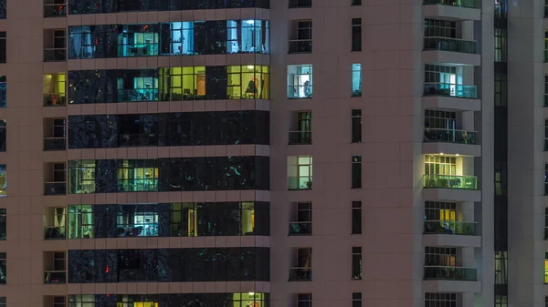 Filas de ventanas brillantes con gente en el edificio de apartamentos por la noche . — Foto de Stock