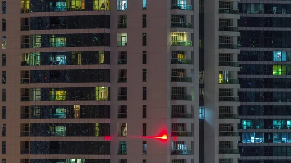 Fileiras de janelas brilhantes com pessoas no prédio de apartamentos à noite . — Fotografia de Stock