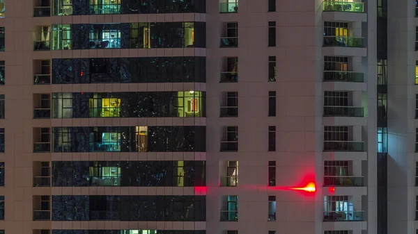 Fileiras de janelas brilhantes com pessoas no prédio de apartamentos à noite . — Fotografia de Stock