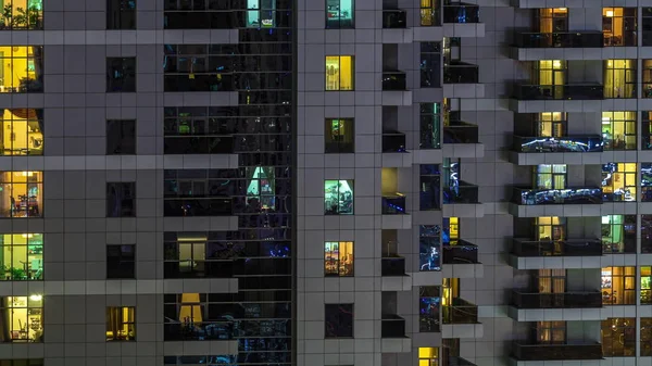 Righe di finestre luminose con persone in condominio di notte . — Foto Stock