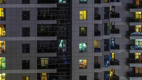 Filas de ventanas brillantes con gente en el edificio de apartamentos por la noche . —  Fotos de Stock
