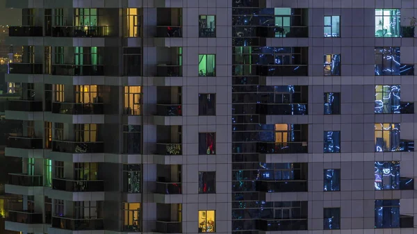 Rijen van gloeiende ramen met mensen in appartementencomplex 's nachts. — Stockfoto