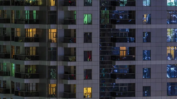 Filas de ventanas brillantes con gente en el edificio de apartamentos por la noche . —  Fotos de Stock