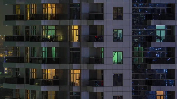 Filas de ventanas brillantes con gente en el edificio de apartamentos por la noche . —  Fotos de Stock