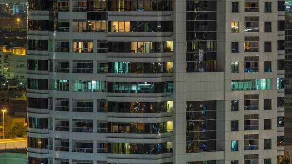Rader av glödande fönster med människor i lägenhetsbyggnad på natten. — Stockfoto