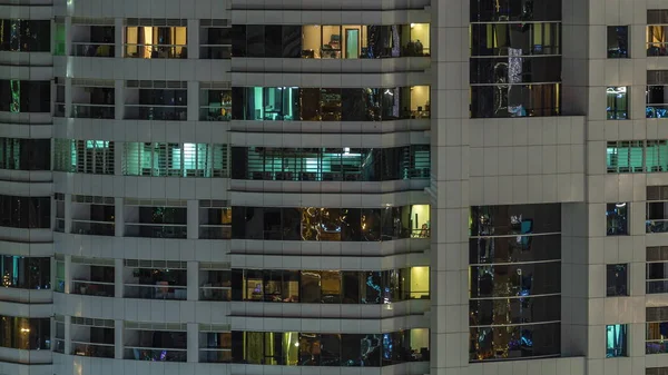 Rows of glowing windows with people in apartment building at night. — Stock Photo, Image