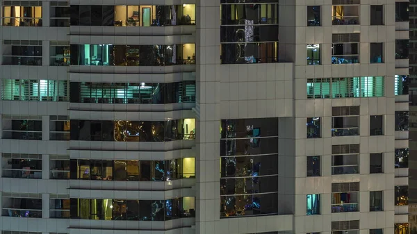 Filas de ventanas brillantes con gente en el edificio de apartamentos por la noche . —  Fotos de Stock