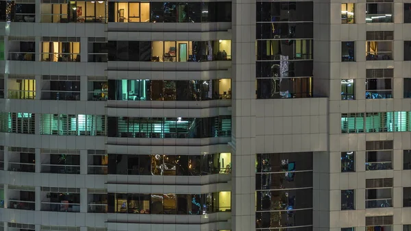 Rijen van gloeiende ramen met mensen in appartementencomplex 's nachts. — Stockfoto