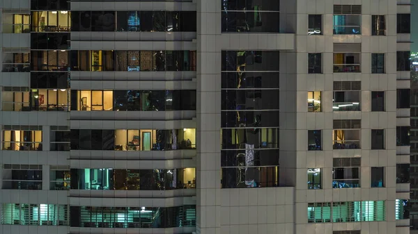 Reihen glühender Fenster mit Menschen in Mehrfamilienhaus in der Nacht. — Stockfoto