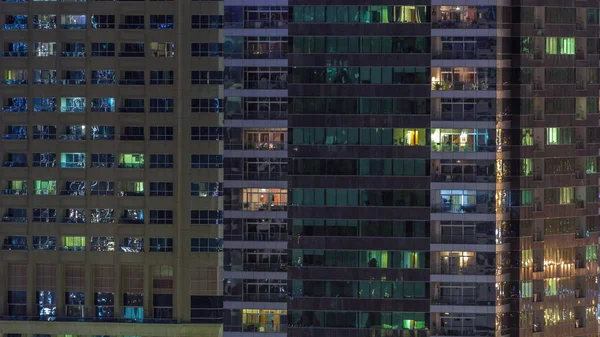 Rijen van gloeiende ramen met mensen in appartementencomplex 's nachts. — Stockfoto