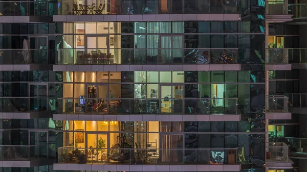 Des rangées de fenêtres rougeoyantes avec des personnes dans l'immeuble la nuit . — Photo