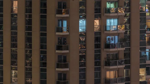 Filas de ventanas brillantes con gente en el edificio de apartamentos por la noche . —  Fotos de Stock