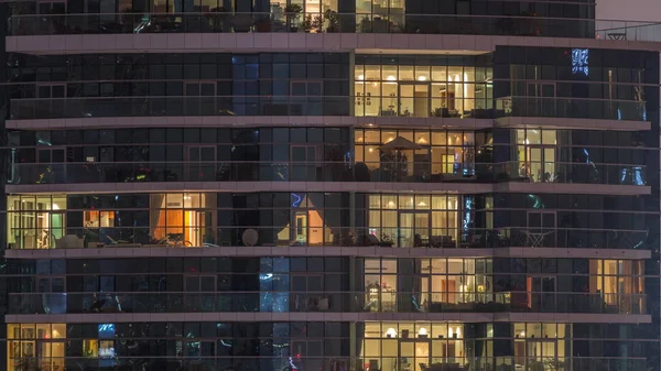 Filas de ventanas brillantes con gente en el edificio de apartamentos por la noche . —  Fotos de Stock