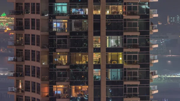 Rijen van gloeiende ramen met mensen in appartementencomplex 's nachts. — Stockfoto