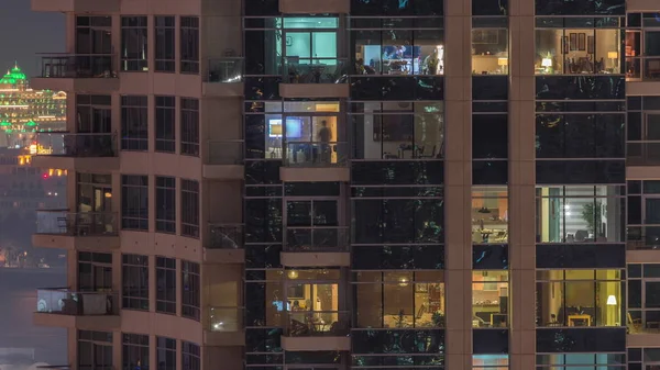 Filas de ventanas brillantes con gente en el edificio de apartamentos por la noche . —  Fotos de Stock