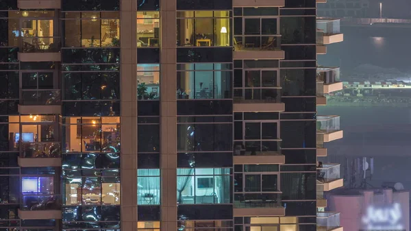 Reihen glühender Fenster mit Menschen in Mehrfamilienhaus in der Nacht. — Stockfoto