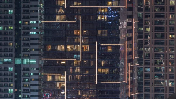 Rader av glödande fönster med människor i lägenhetsbyggnad på natten. — Stockfoto
