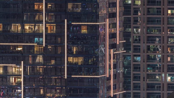 Filas de ventanas brillantes con gente en el edificio de apartamentos por la noche . —  Fotos de Stock