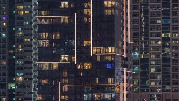 Filas de ventanas brillantes con gente en el edificio de apartamentos por la noche . —  Fotos de Stock