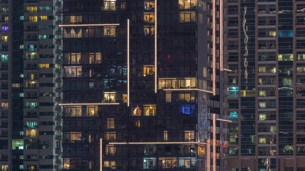 Filas de ventanas brillantes con gente en el edificio de apartamentos por la noche . —  Fotos de Stock