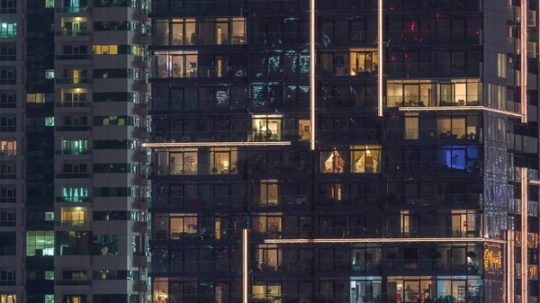 Γραμμές από λαμπερά παράθυρα με τους ανθρώπους στην πολυκατοικία τη νύχτα. — Φωτογραφία Αρχείου